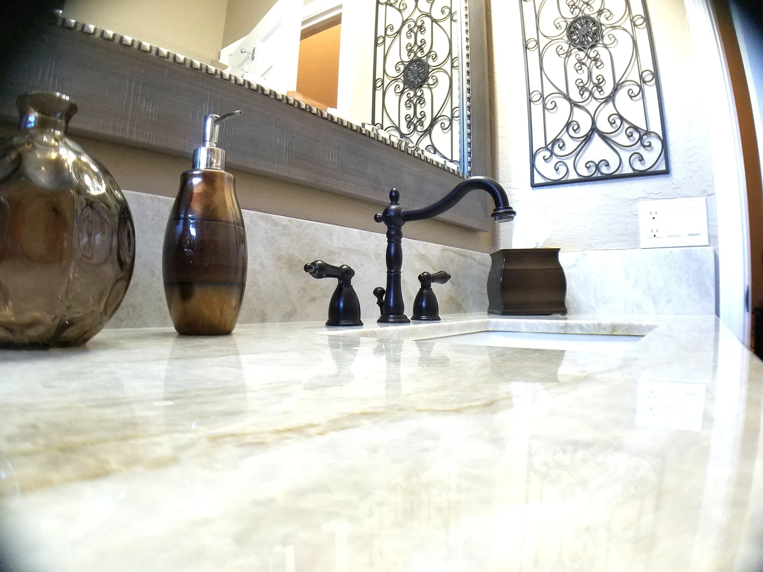 Pale quartzite bathroom vanity top with an undermount basin, oil-rubbed bronze faucet and a framed silver mirror